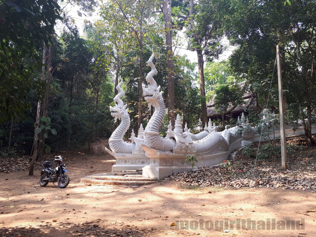 a huge white temple entrance with naga dragon snakes and a motorcycle. Motogirlthailand