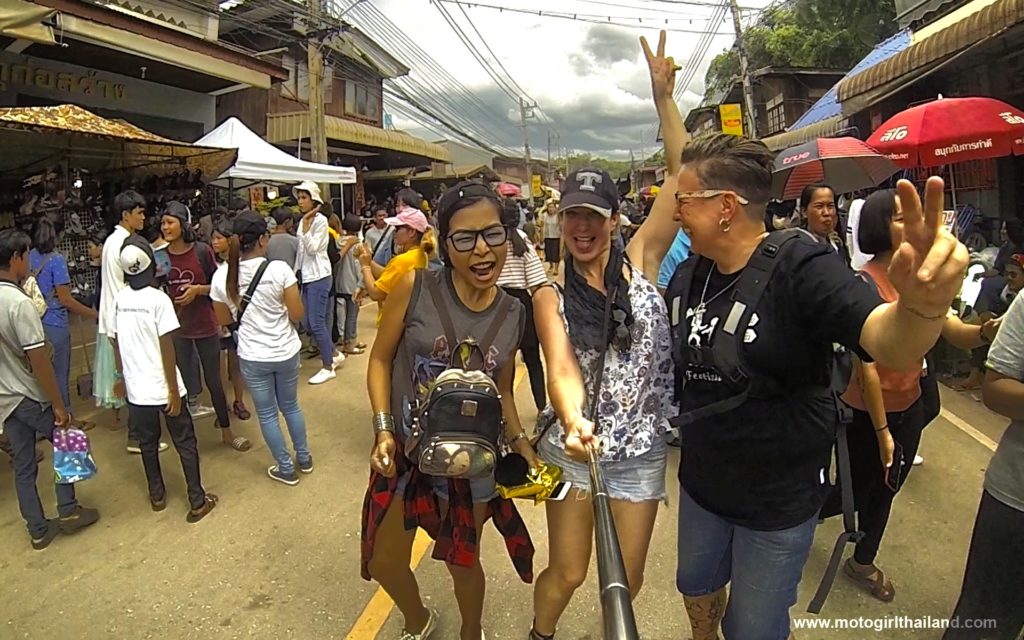 three ladies laughing into a camera with a crowd of people in the background. motogirlthailand