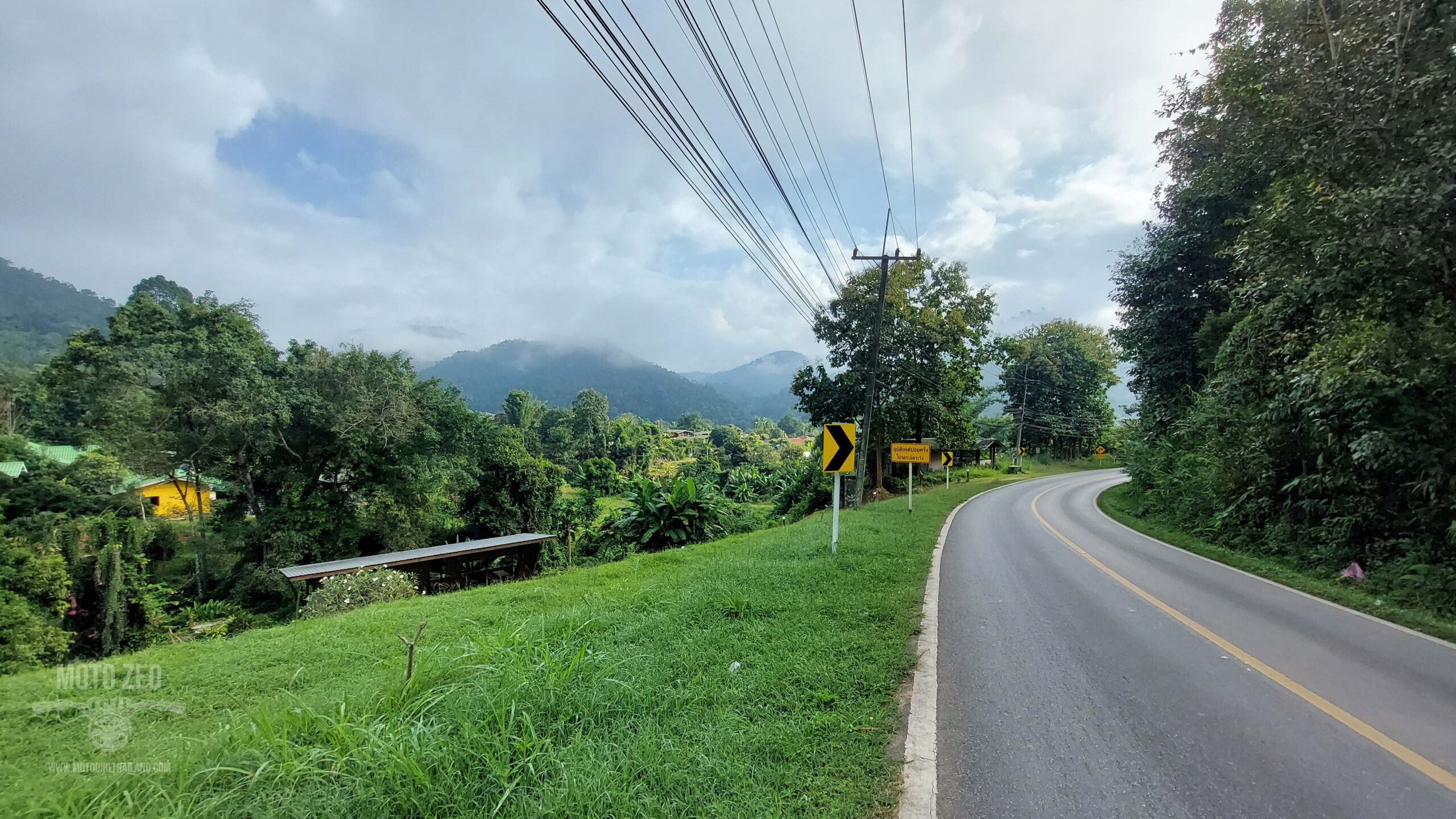 a sweeping road surrounded by trees and a mountain in the background. Northern Thailand