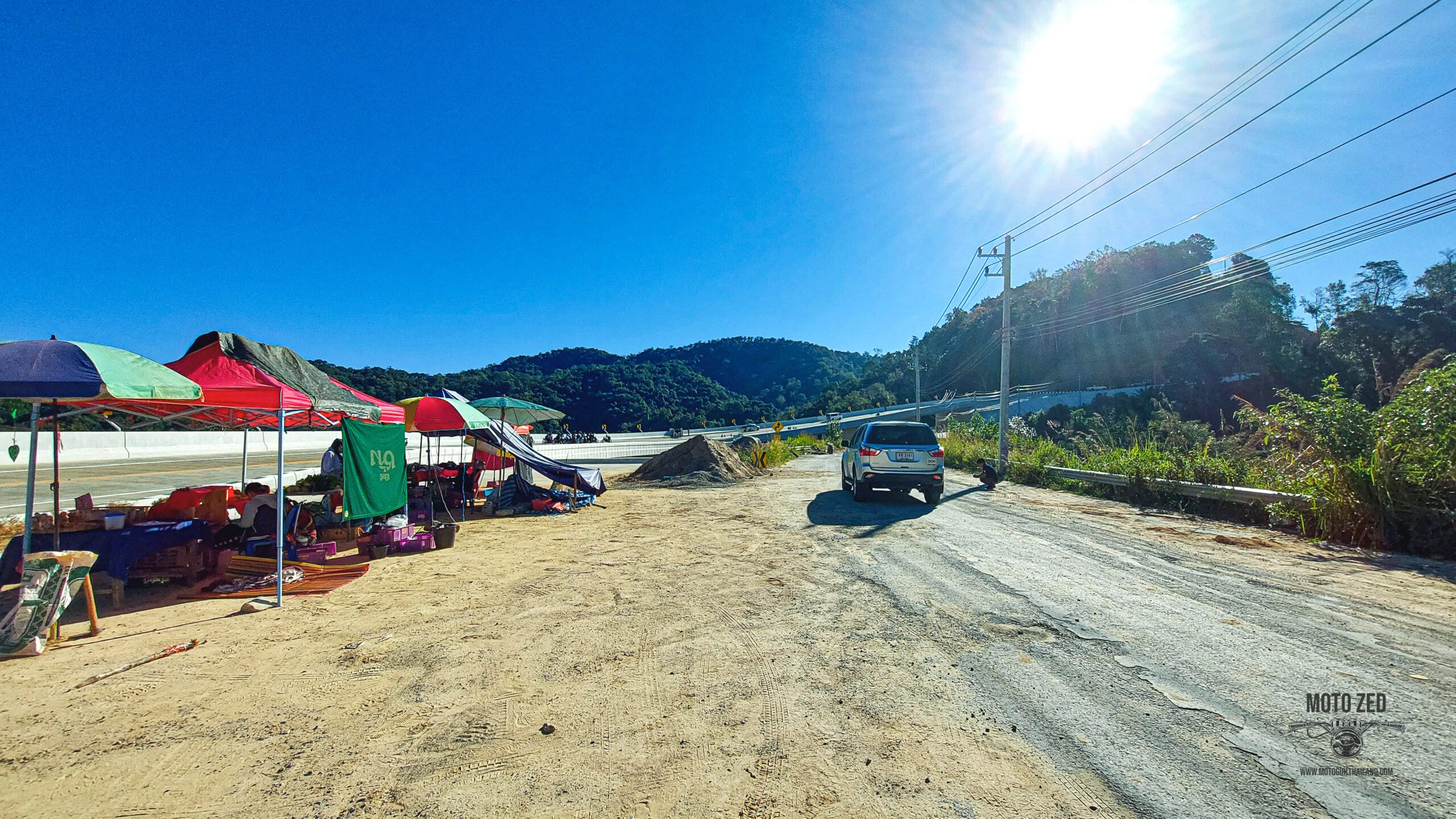 dirt road with stalls at the side and a road leading into the mountains.