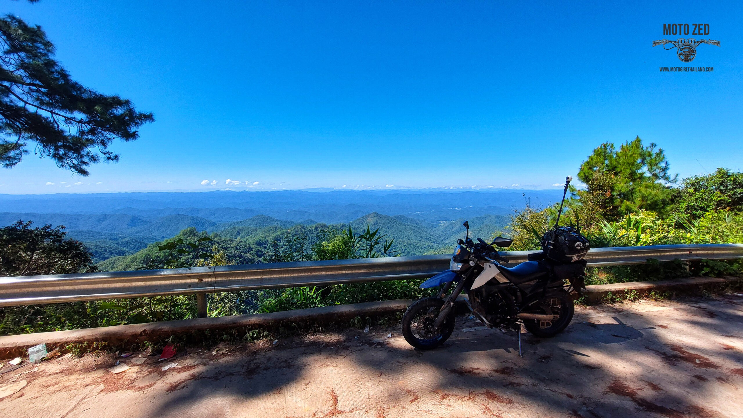 motorcycle with a 360 camera mount at a viewpoint with mountains and shadows and trees. The sunlight is strong and the horizon shows many mountain ridges.