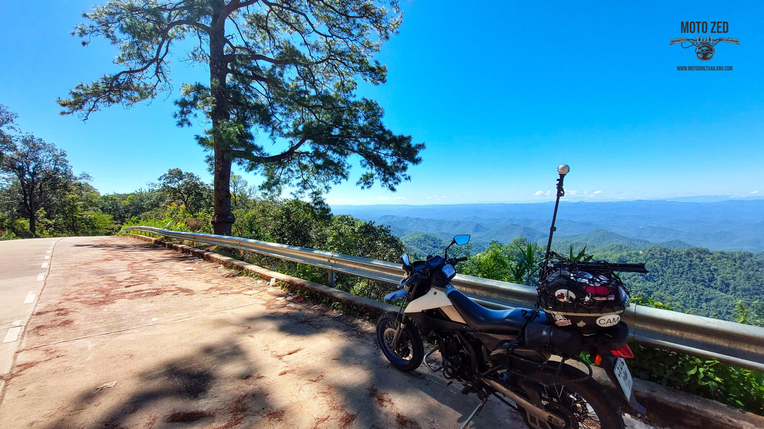 motorcycle with a 360 camera mount at a viewpoint with mountains and shadows and trees. The sunlight is strong and the horizon shows many mountain ridges.