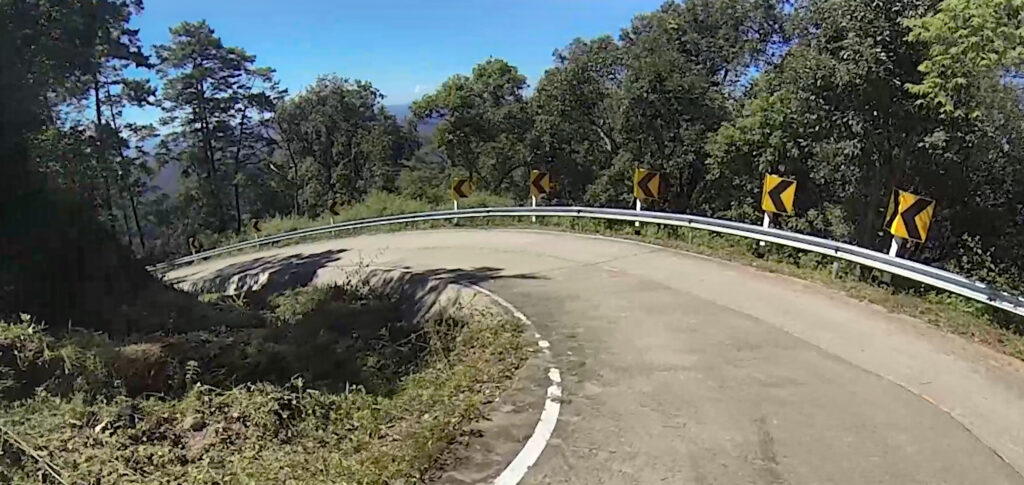 a super twisty road surrounded by green trees and blue sky. Northern Thailand