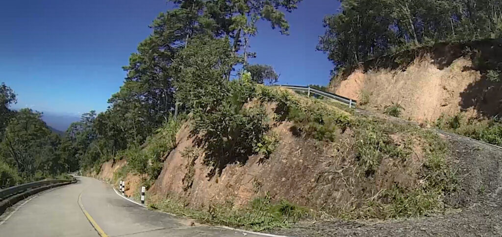 a super twisty road surrounded by green trees and blue sky. Northern Thailand